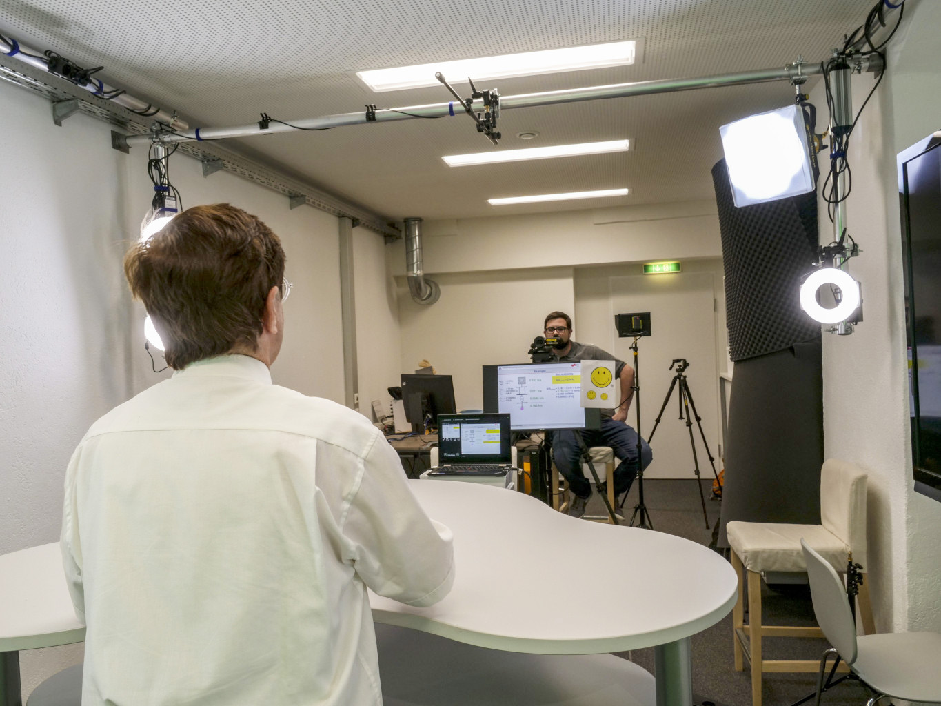 Videodreh im Studio. Ein Lehrender von hinten, er blickt in die Kamera mit Teleprompter.