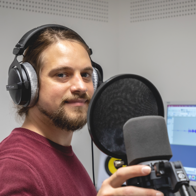 Foto von Martin Haiden: Er sitzt mit Kopfhörern im Tonstudio neben einem Mikrofon mit Popschutz