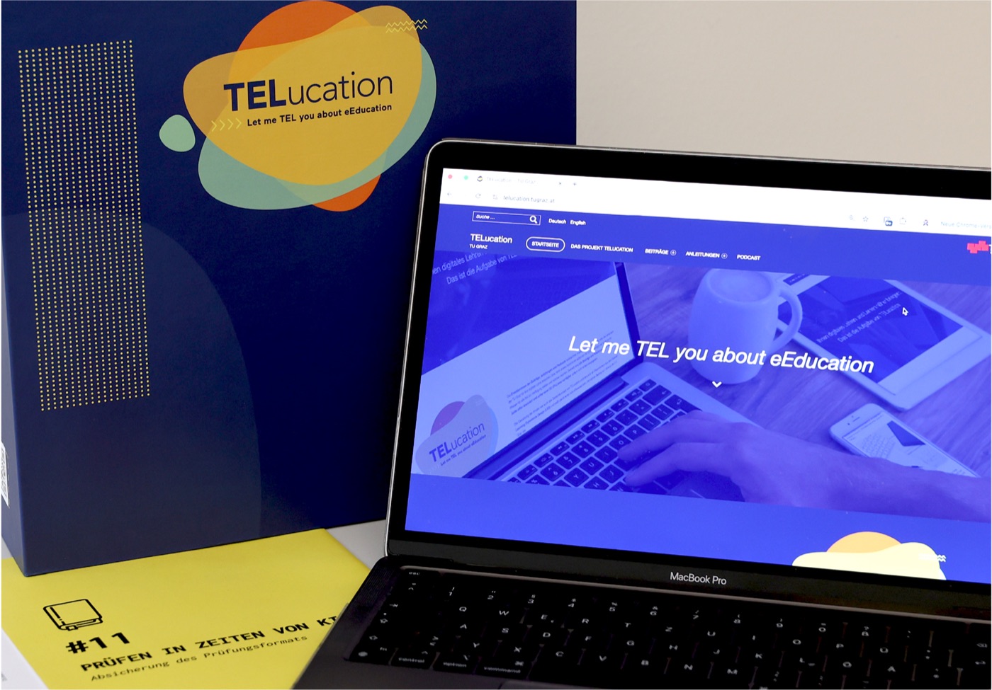 Die TELucation-Website auf einem Laptop, daneben die Sammelmappe.